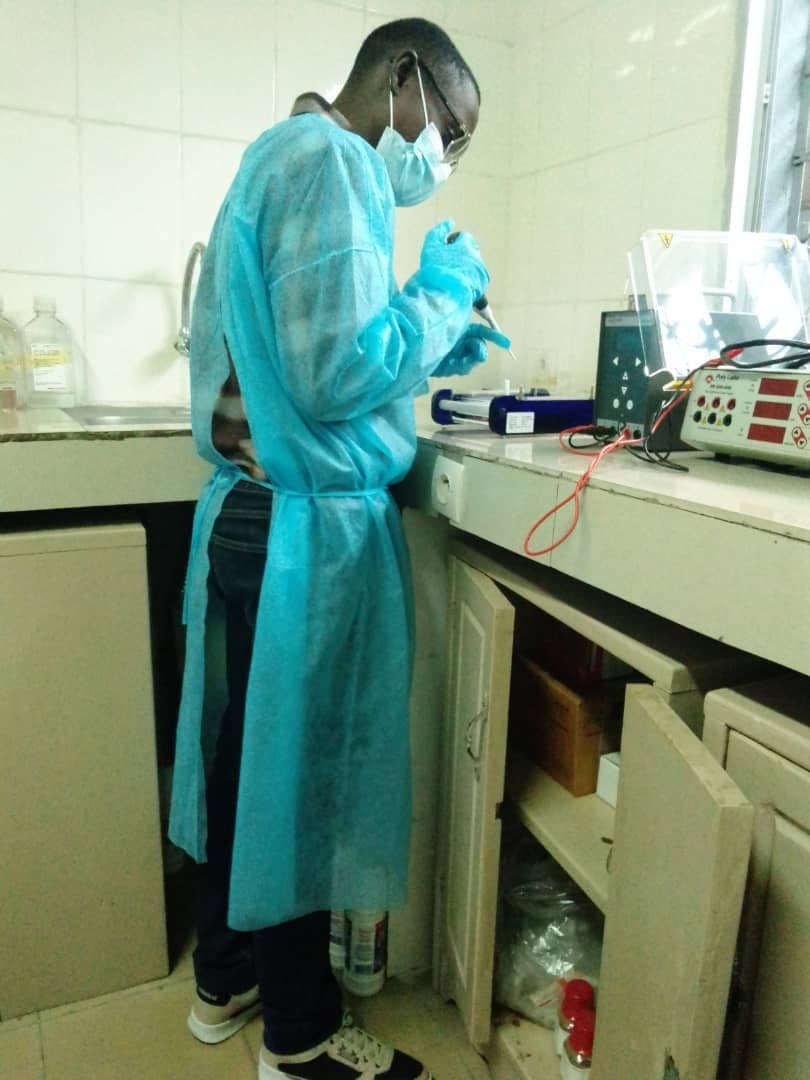 A researcher in protective gear pipetting samples at a laboratory bench.